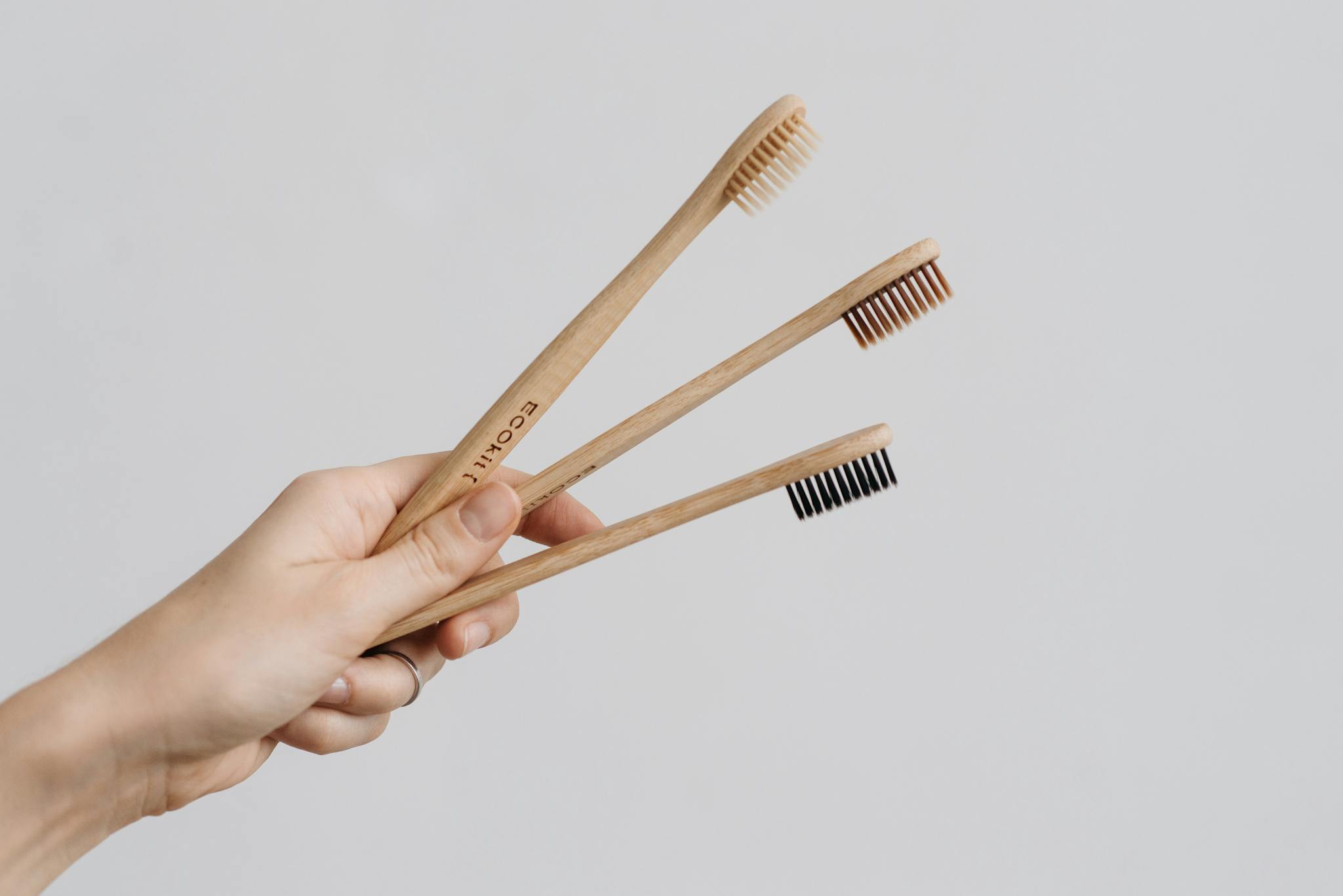 Close-up of a hand holding eco-friendly wooden toothbrushes against a white background.