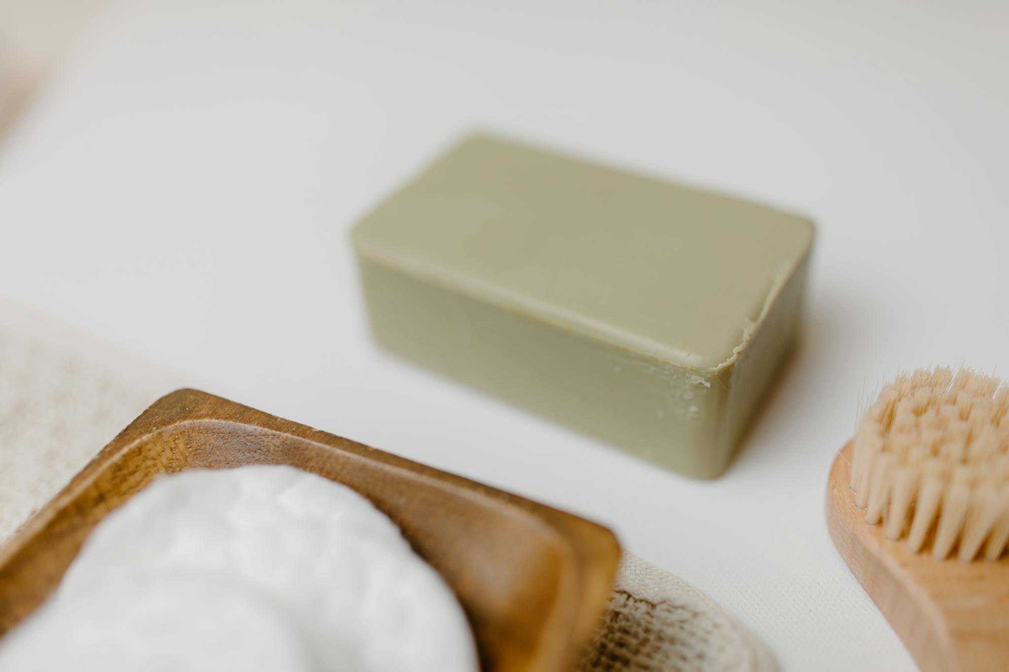 Close-up of a natural soap bar with a wooden brush and cotton pads for skincare.