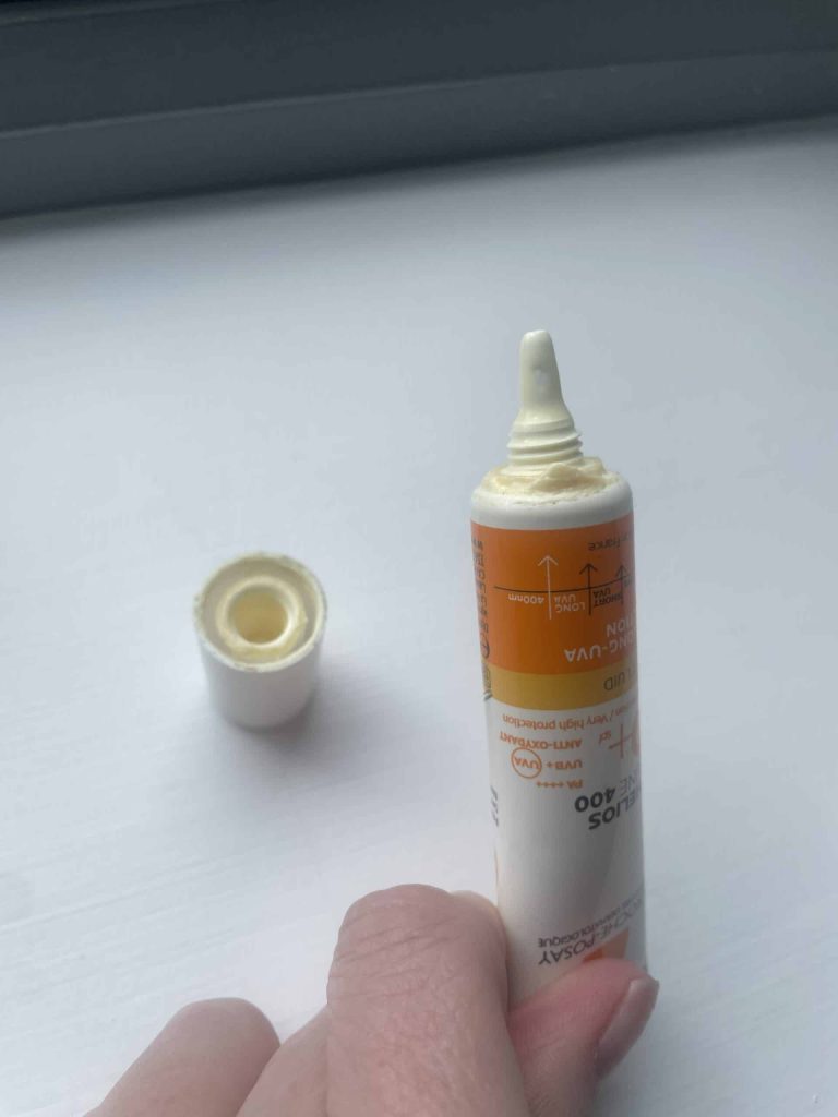 A close-up view of the fine precision dropper nozzle tip of a La Roche-Posay sunscreen tube, showing a drop of light yellow fluid texture