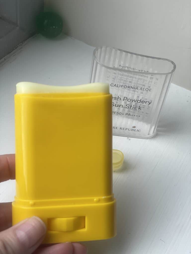 An opened yellow Nature Republic sun stick tube showing the curved, creamy white solid sunscreen balm with the clear cap sitting in the background.